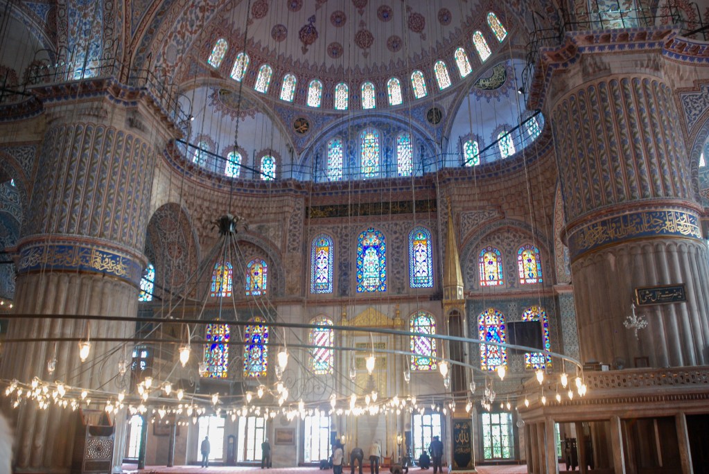 Inside the Blue Mosque, light pours through stained glass and settles gently across domes, columns, and prayer rugs.