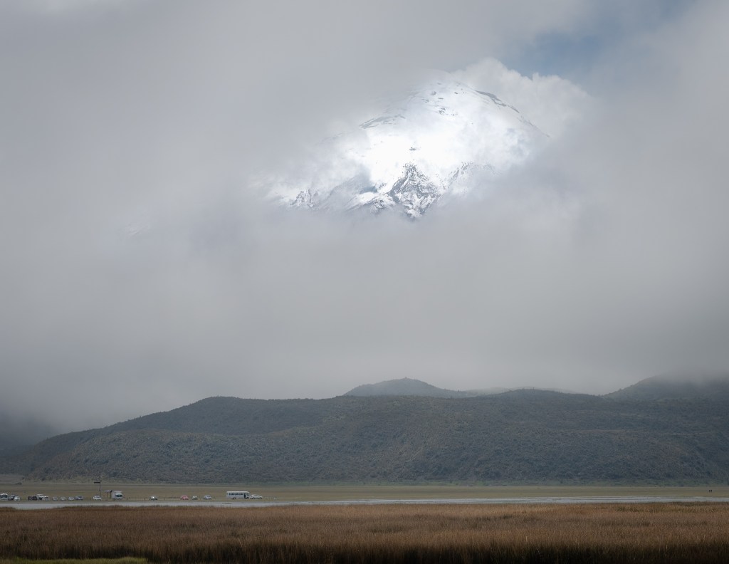 Near the base in Cotopaxi National Park, the summit glows faintly through a veil of mist while the páramo grasslands stretch across the high volcanic plain.