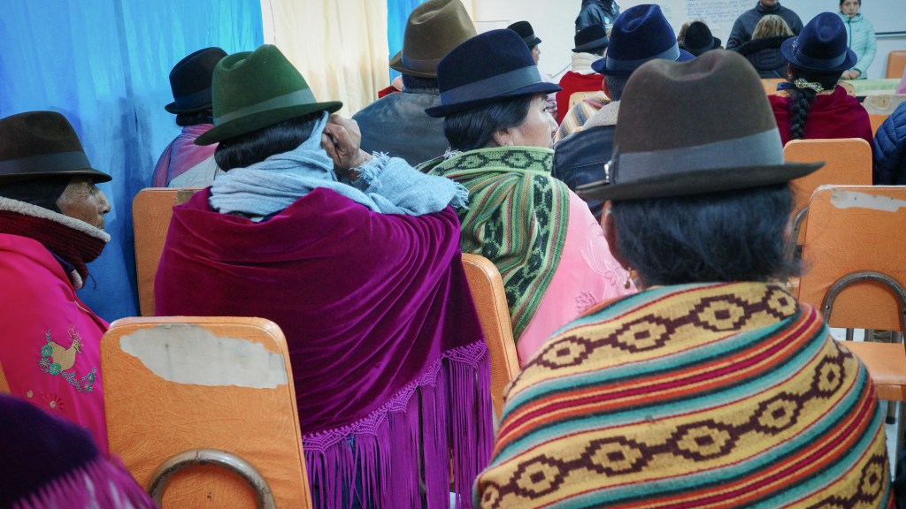 Inside a village building above Quilotoa crater lake, Kichwa community members gather for a meeting with visiting volunteers. Woven textiles and felt hats create a vivid tapestry of color in the high Andes.