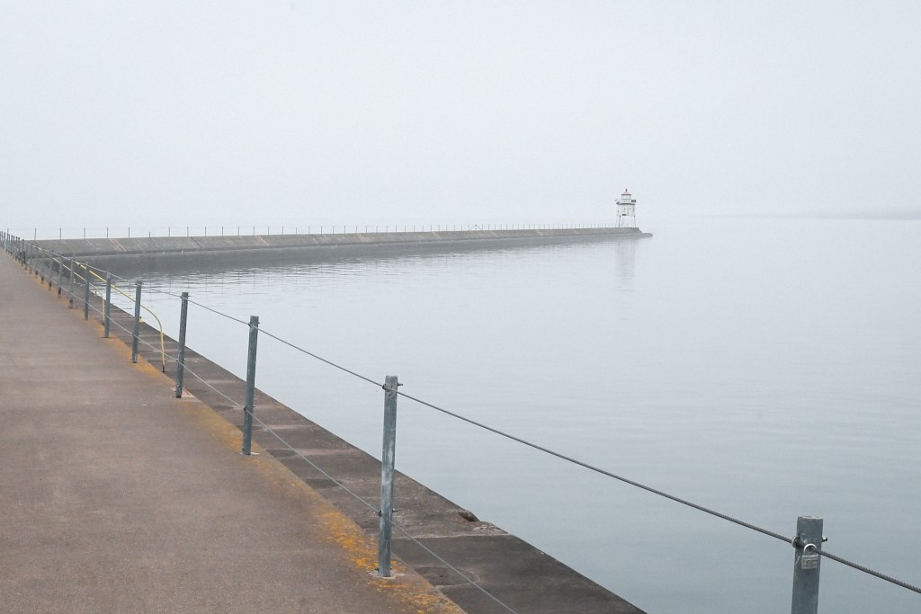 The breakwater for two harbors Minnesota narrows until it reaches the small lighthouse - fading into the mist